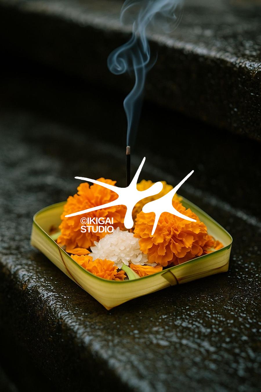 Canang sari offering with marigolds and burning incense on a wet stone step