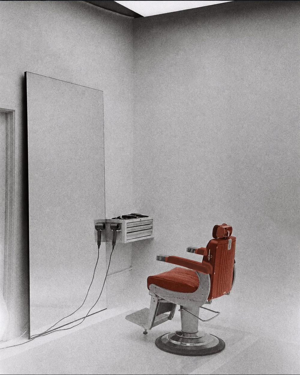 Editorial view of minimalist barber station with burnt orange chair and leaning mirror