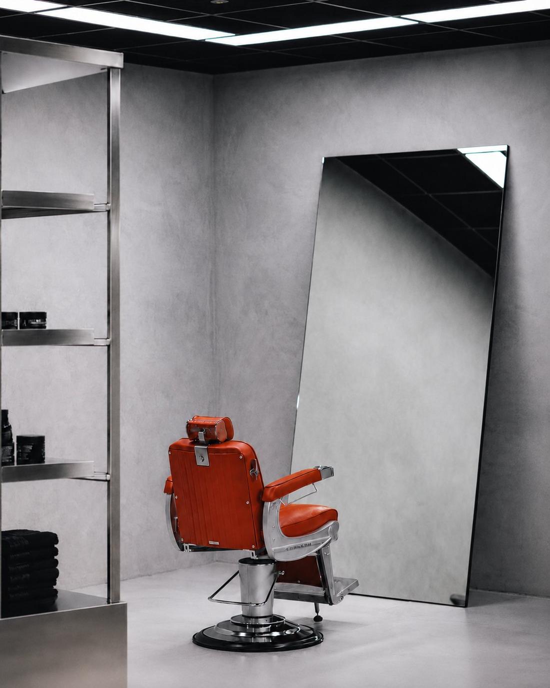Burnt orange barber chair with stainless steel shelving and large leaning mirror